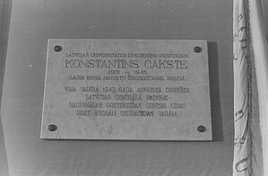 Latviešu fotogrāfa Andra Dzeņa nofotogrāfēta LU prof. Konstantīna Čakstes piemiņas plāksne ar latviešu studentu vienības Austrums karogu labajā pusē LU Mazajā aulā, 27.09.1994. Foto: no LU Muzeja krājuma